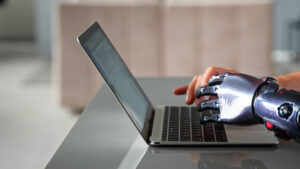 Black bio limb prothesis and healthy hand appear over laptop and type on keyboard under bright sunlight