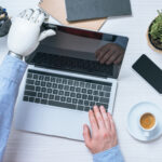 partial view of businessman with prosthetic arm opening laptop at table in office