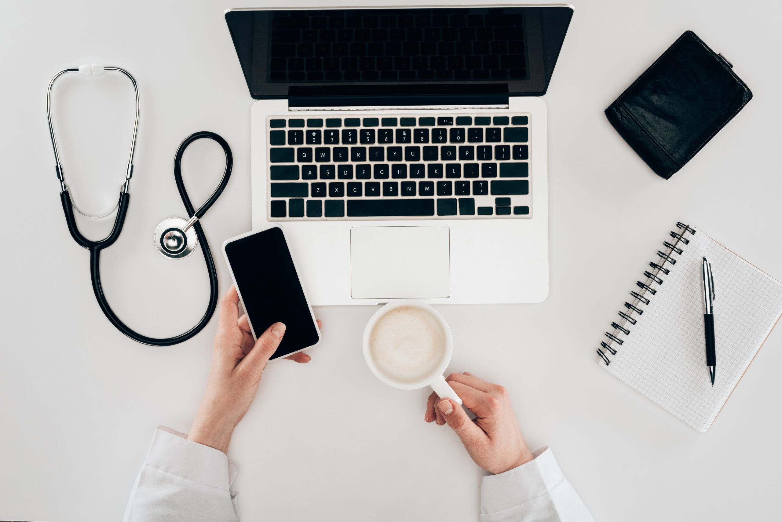 partial view of doctor at workplace with laptop, stethoscope and cup of coffee